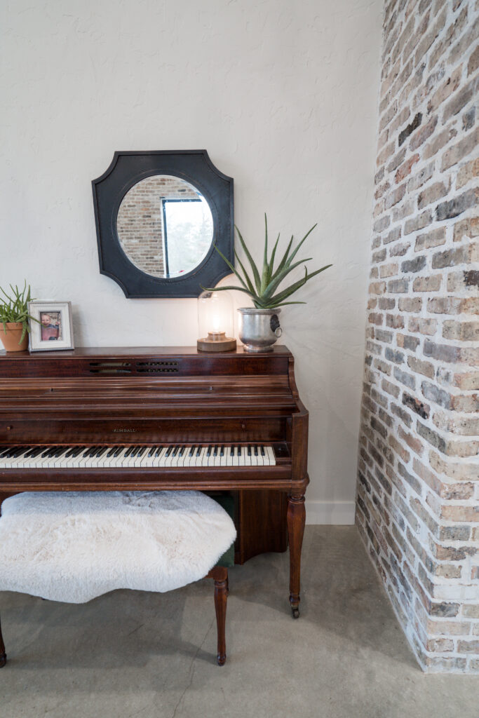 A brown piano with a mirror above and two plants and a frame on the piano
